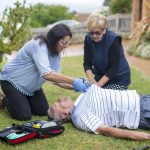 Two women prepare to attach an AED to a man who has collapsed on the ground.