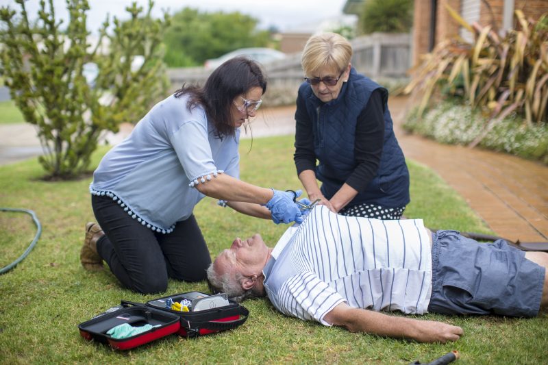 Two women prepare to attach an AED to a man who has collapsed on the ground.