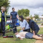 Two paramedics approaching a patient on the ground who is being assisted by two people.