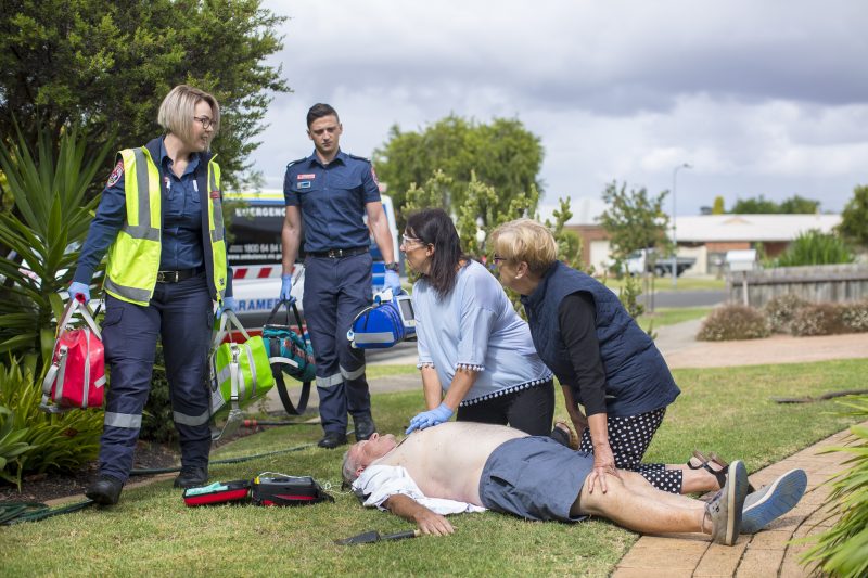 Two paramedics approaching a patient on the ground who is being assisted by two people.