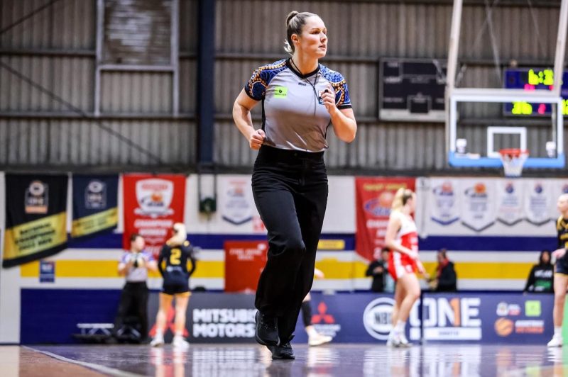 A woman referee runs down a basketball court.