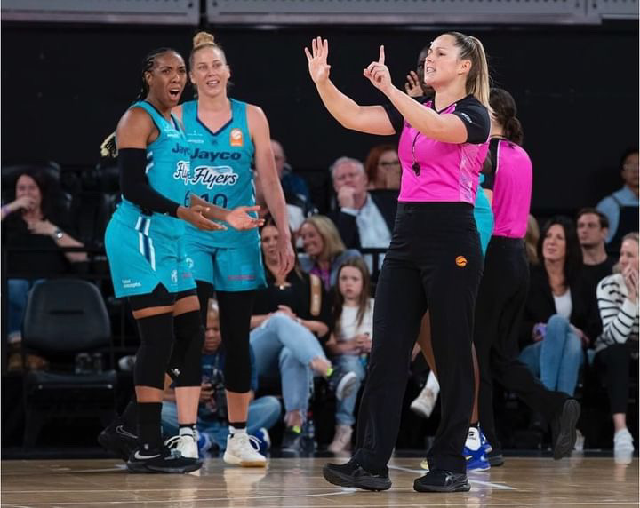 A woman referee signals a call in front of disgruntled WNBL players.