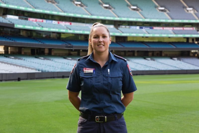 A woman paramedic on the ground at the MCG, smiling for the camera.