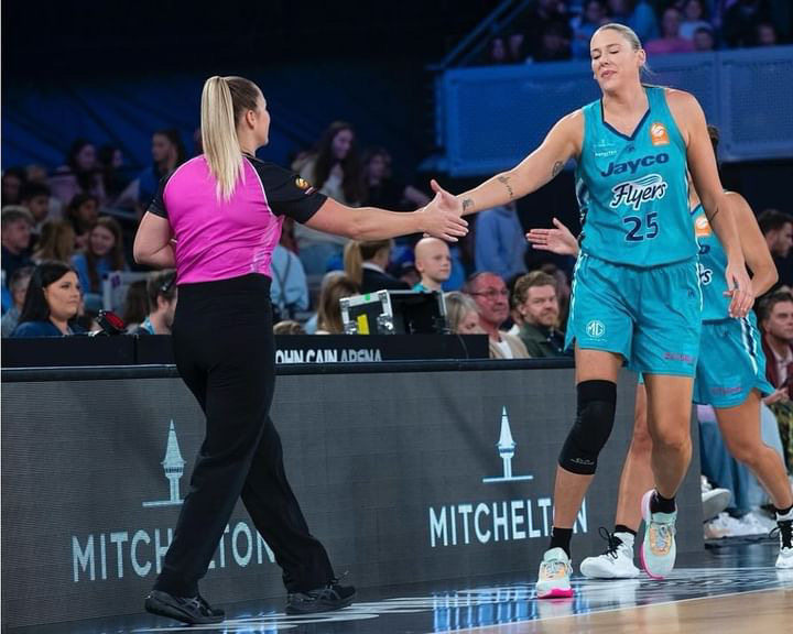 A woman referee shakes hands with a WNBL player.