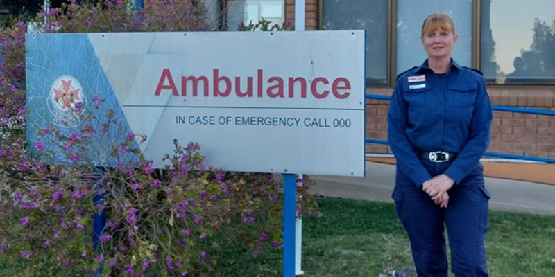 A woman is standing beside a signage for the ambulance branch located in front of a building