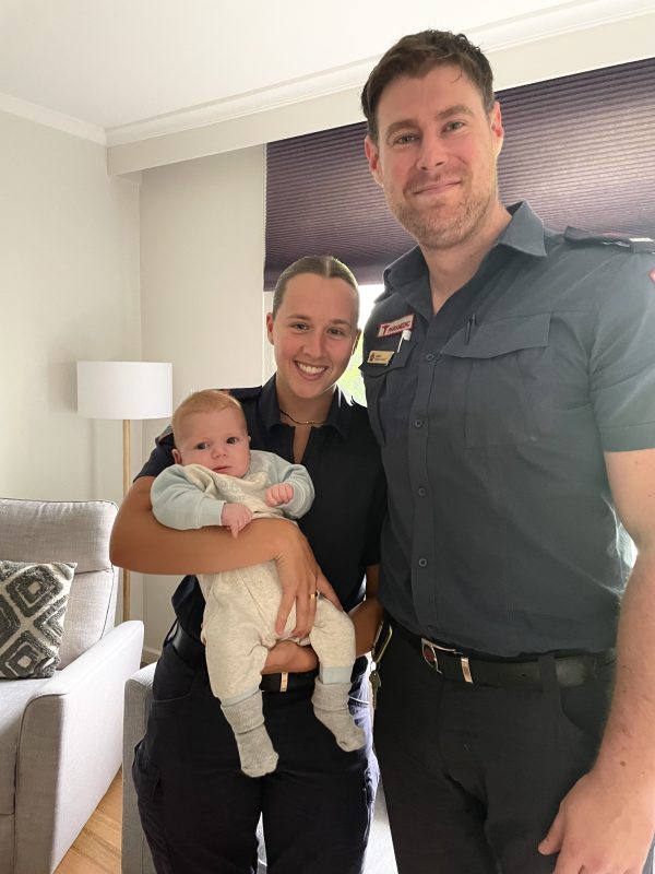 Two paramedics smile for the camera, holding a baby.