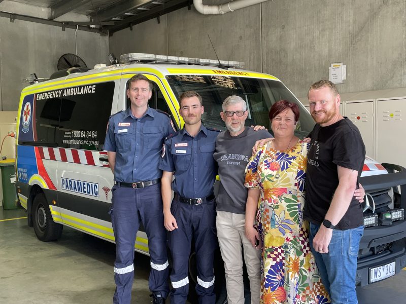 A group of smiling people standing in front of an ambulance.