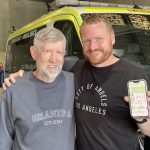 Two men standing side by side and one is holding up an iphone.