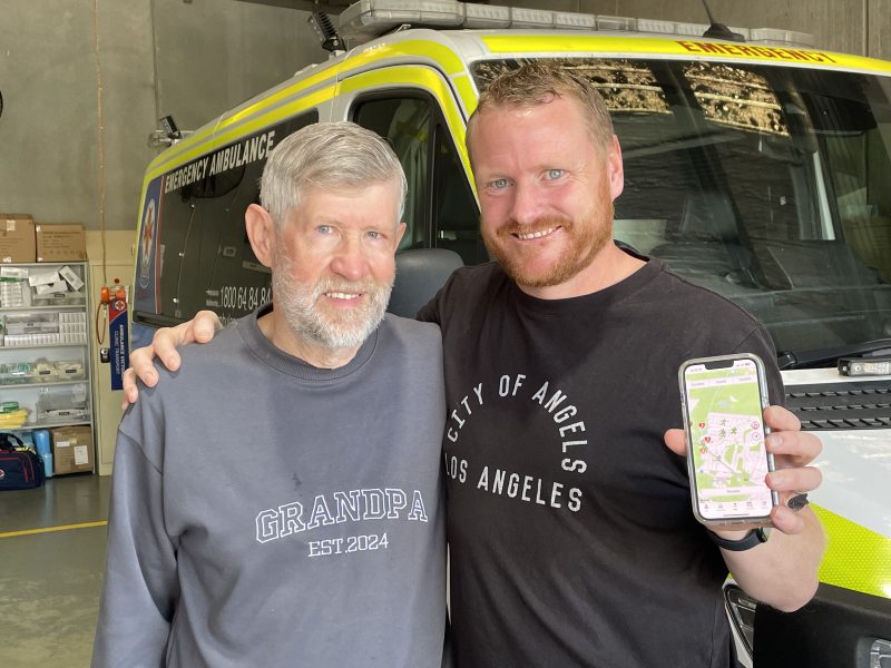 Two men standing side by side and one is holding up an iphone.