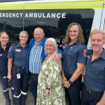 A group of people standing in front of an ambulance.