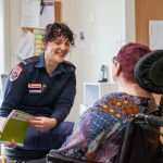 An Ambulance Victoria paramedic smiles towards a person in a wheelchair, who has their back to the camera.