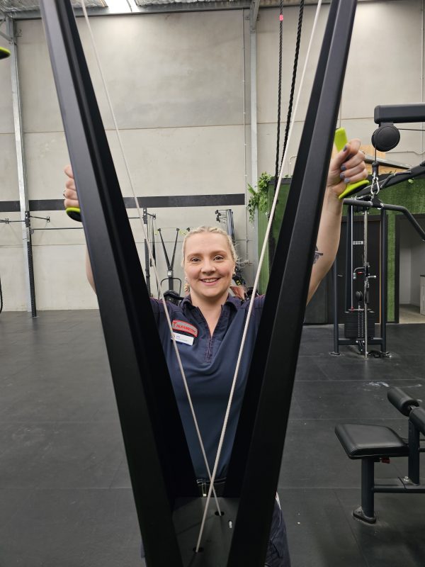 A woman in Ambulance Victoria paramedic uniform smiles for the camera at the SkiErg machine.