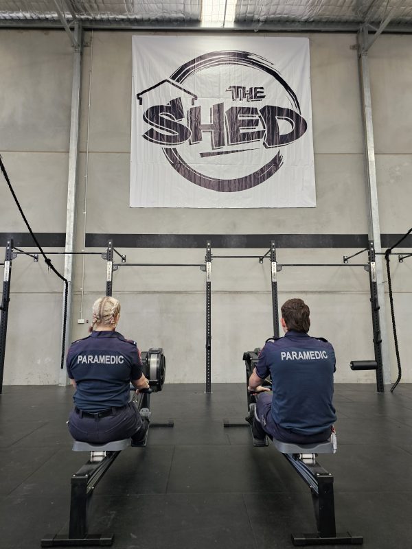 Two people sit on rowing machines in The Shed Gym with their backs to the camera. 'PARAMEDIC' is written on the back of their tops.