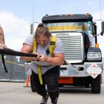 A woman pulls a big truck forward using a rope.