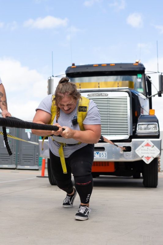 A woman pulls a big truck forward using a rope.