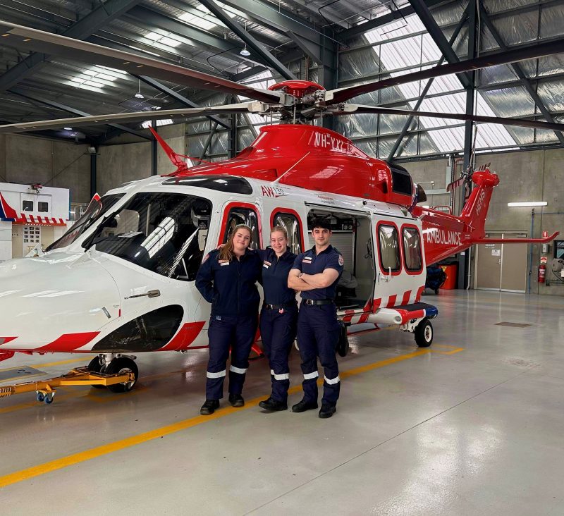 Three paramedics smile for the camera in front of an Ambulance Victoria helicopter.