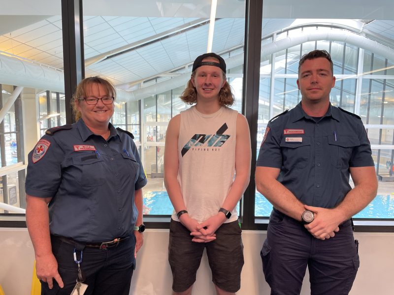 Two paramedics stand either side of a teenage boy at an aquatic centre.