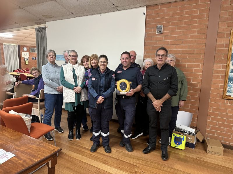 Two paramedics holding a training AED stand with a group of people from the Rochester Senior Citizens Club.