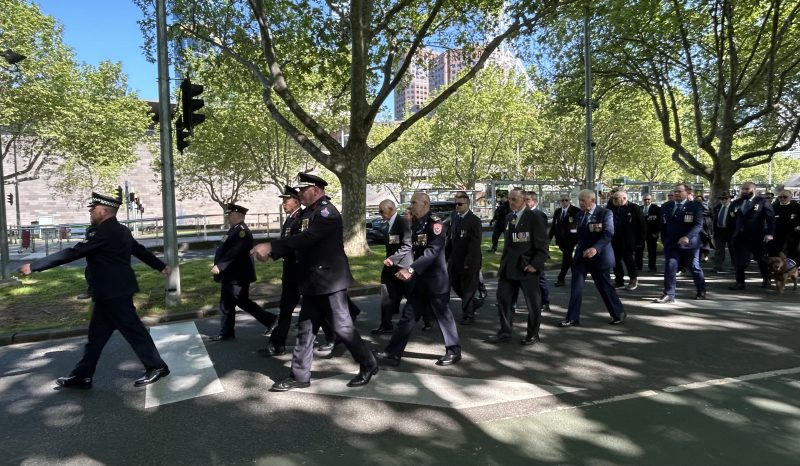 Uniformed people, many with medals pinned to their jackets, march along St Kilda Rd in Melbourne. It's a sunny day.