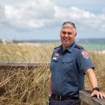 A male paramedic standing in front of grass at the beach.