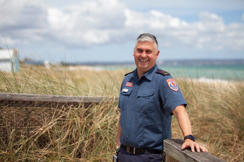 A male paramedic standing in front of grass at the beach.