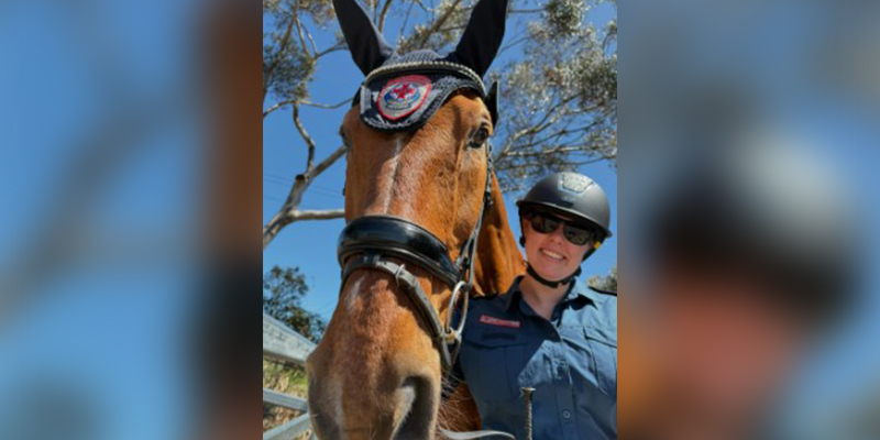 A woman in uniform and wearing a helmet is standing beside a horse.