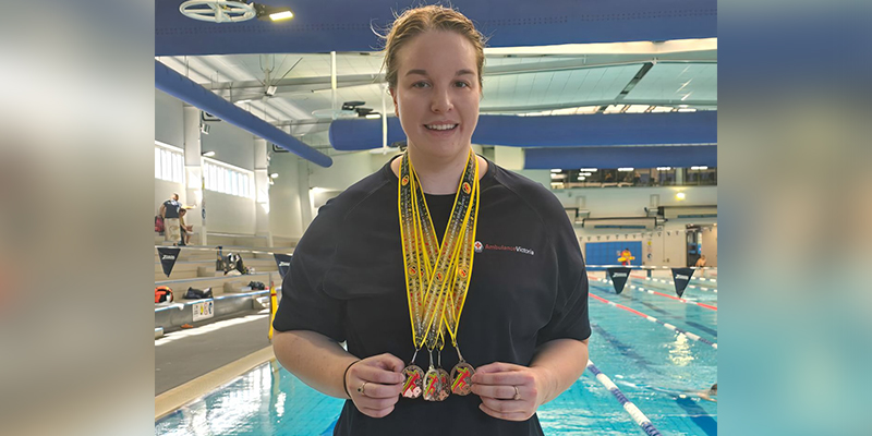 A woman is standing beside a swimming pool, holding three medals hanging around her neck.