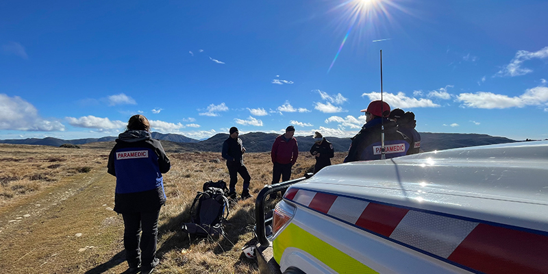 A group of paramedics are standing in a open area with mountains in the background.