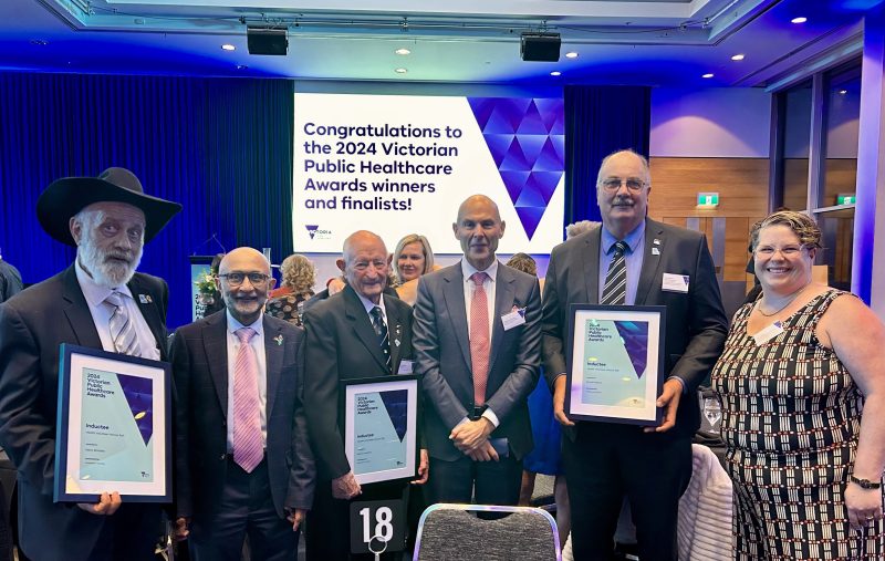 Five men and one woman smile for the camera at the Victorian Public Healthcare Awards event. Three of the men hold certificates.