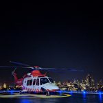 An ambulance helicopter is on a helipad. It's night time and the city is in the background.