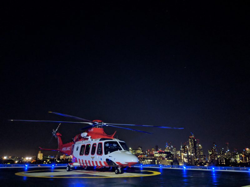 An ambulance helicopter is on a helipad. It's night time and the city is in the background.