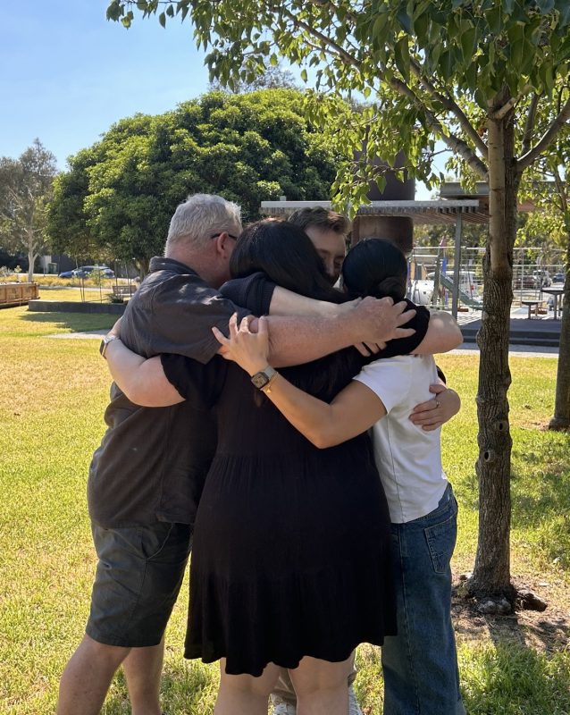 Four people hugging in a park.