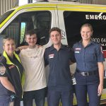 Four people smiling in front of an ambulance.