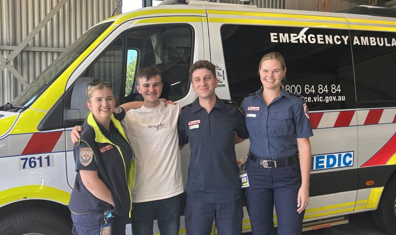 Four people smiling in front of an ambulance.