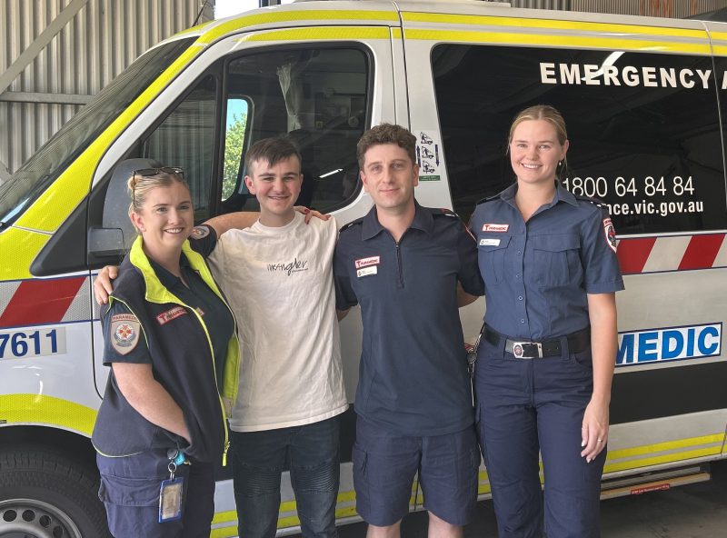 Four people smiling in front of an ambulance.