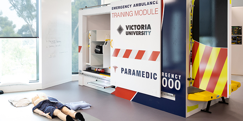 A manikin lies on the floor in front of a emergency ambulance training module used by students for simulations.