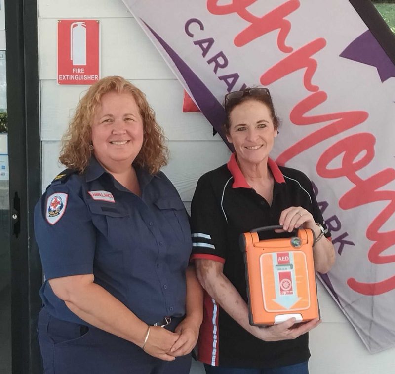 Two women standing in front of a sign. One is holding a defibrillator.