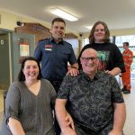 MICA Paramedic Angus Bowden, smiling at camera with his patient Phil Stockton and his wife and son.