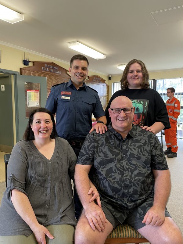 MICA Paramedic Angus Bowden, smiling at camera with his patient Phil Stockton and his wife and son.