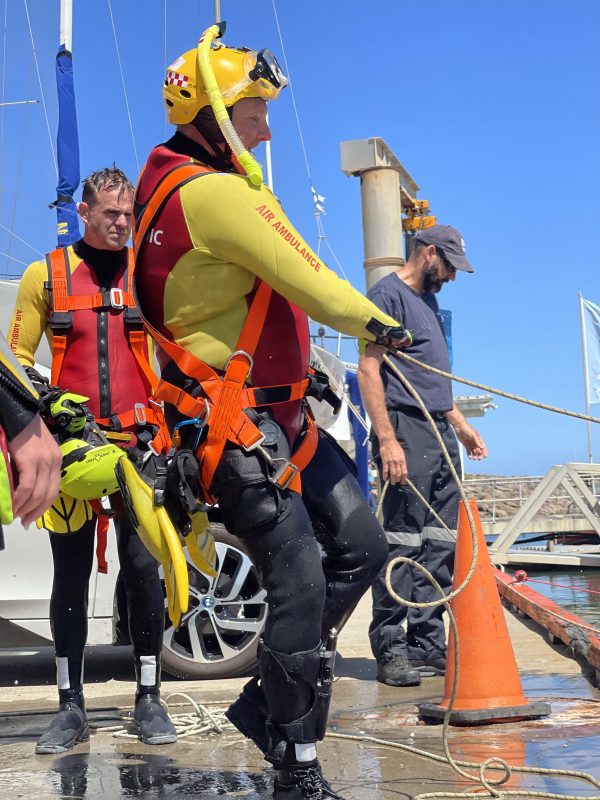 A man in a wetsuit, helmet, snorkle and googles pulling on a rope off the side of a jetty