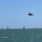 The air ambulance helicopter flying low over a body of water, yachts are sailing below