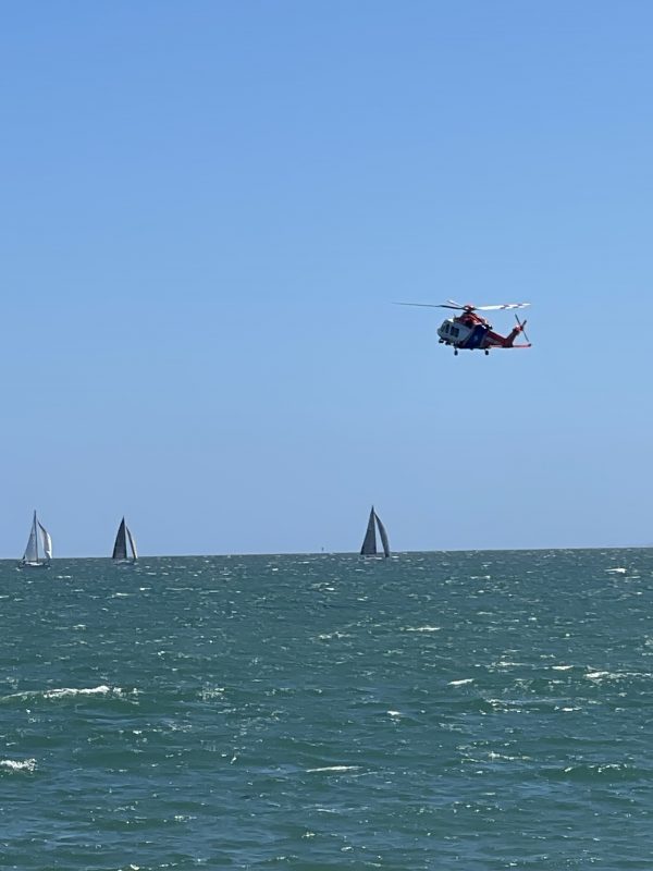 The air ambulance helicopter flying low over a body of water, yachts are sailing below