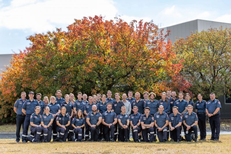 A large group of paramedics in front of a tree.