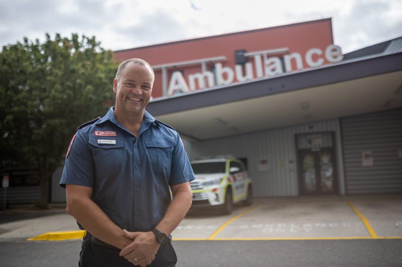 A male paramedic standing in front of an ambulance building.