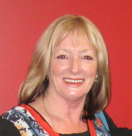 A headshot of a blonde woman who smiles at the camera, in front of a red background.