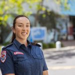 A brown-haired woman in paramedic uniform smiles for the camera.