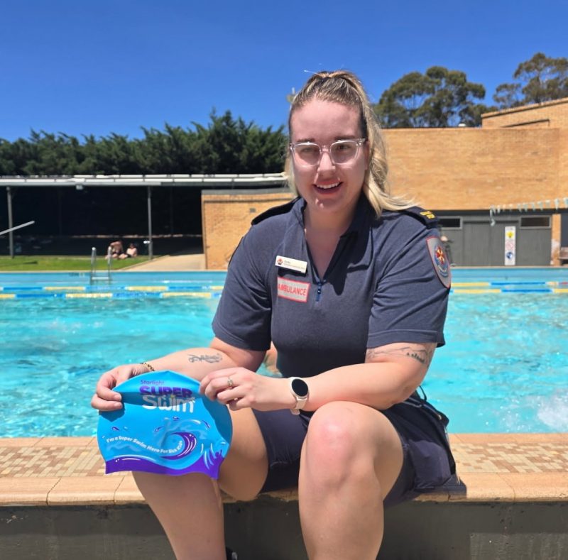 A paramedic sitting next to the pool holding a swimming cap.