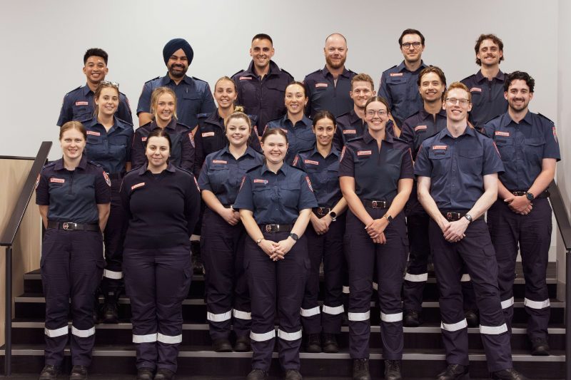 A group of 20 paramedics smile for the camera. They are standing in rows on a set of wide stairs.