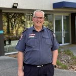 Paul in uniform, smiling and standing in front of an ambulance building