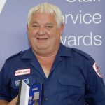 A man in Ambulance Victoria uniform smiles at the camera holding an award.